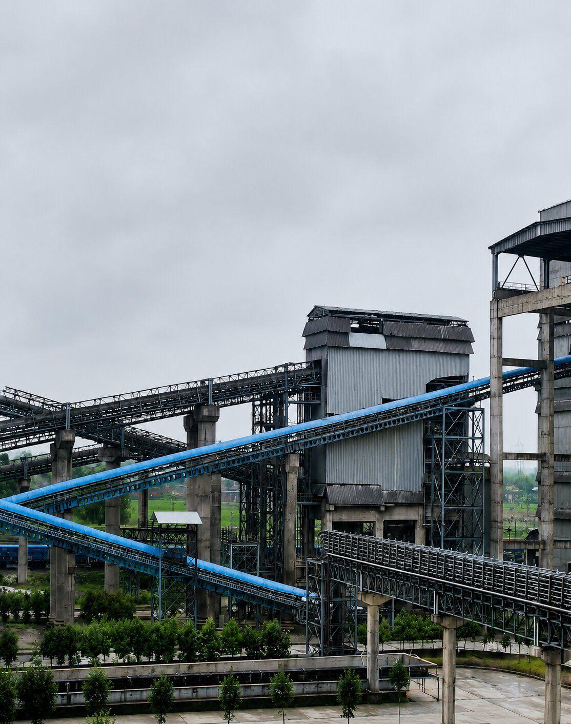 Industrial complex with interconnected buildings and blue conveyor belts under a cloudy sky.