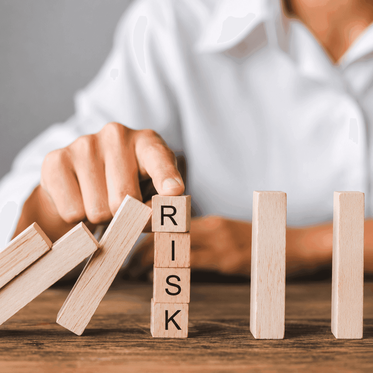 Hand stopping falling dominoes spelling 'RISK', preventing a chain reaction.