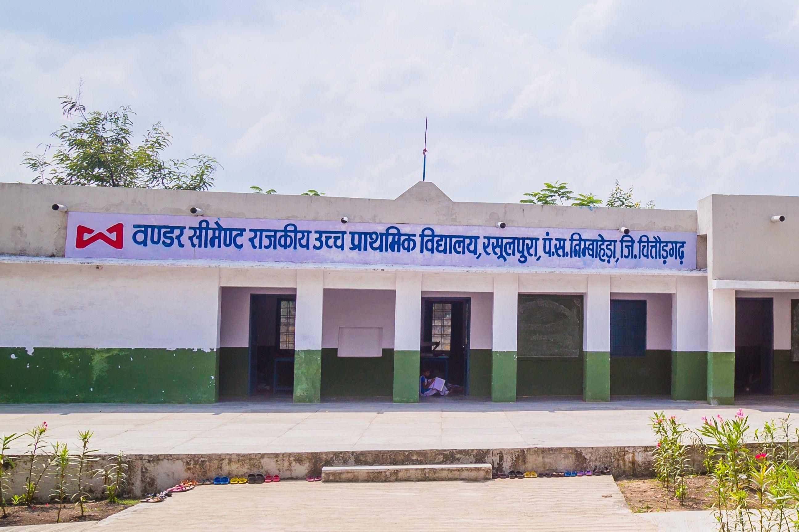 Front of a white and green school building with a sign displaying Hindi text.