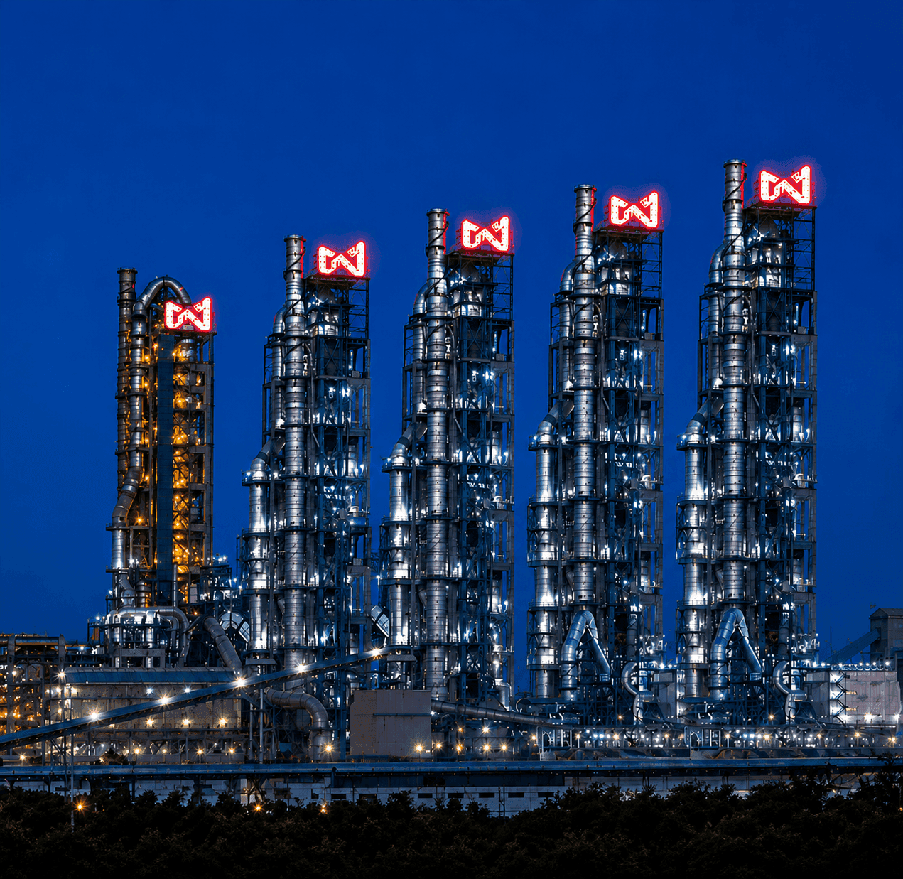 Modern industrial towers with glowing red logos stand illuminated against the dark night sky.