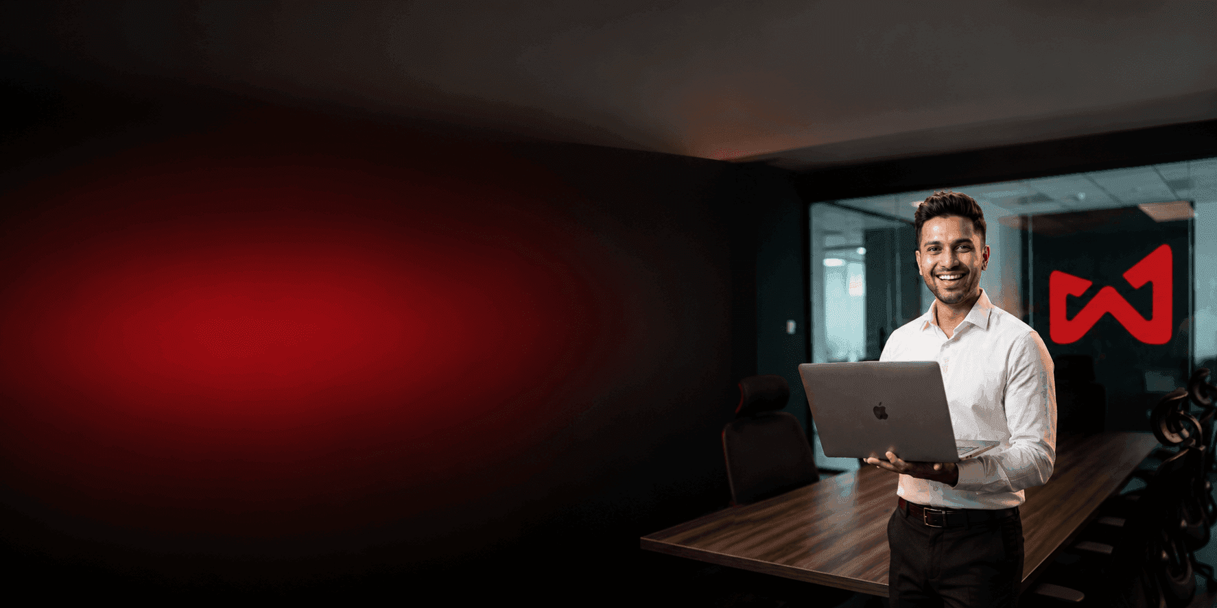 Smiling man holds laptop in modern office meeting room with red W logo.