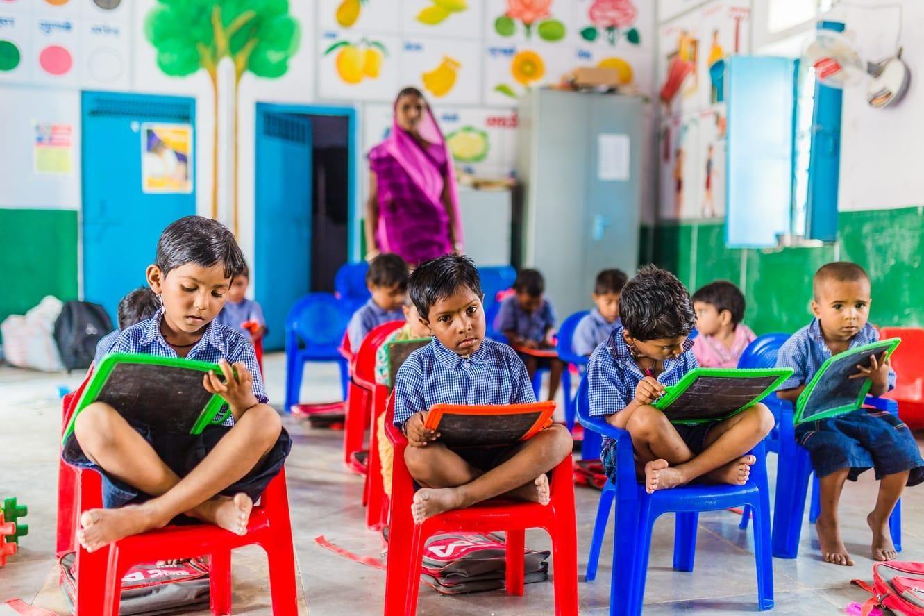 Young children in uniforms learn by writing on slates in a vibrant classroom with a teacher.