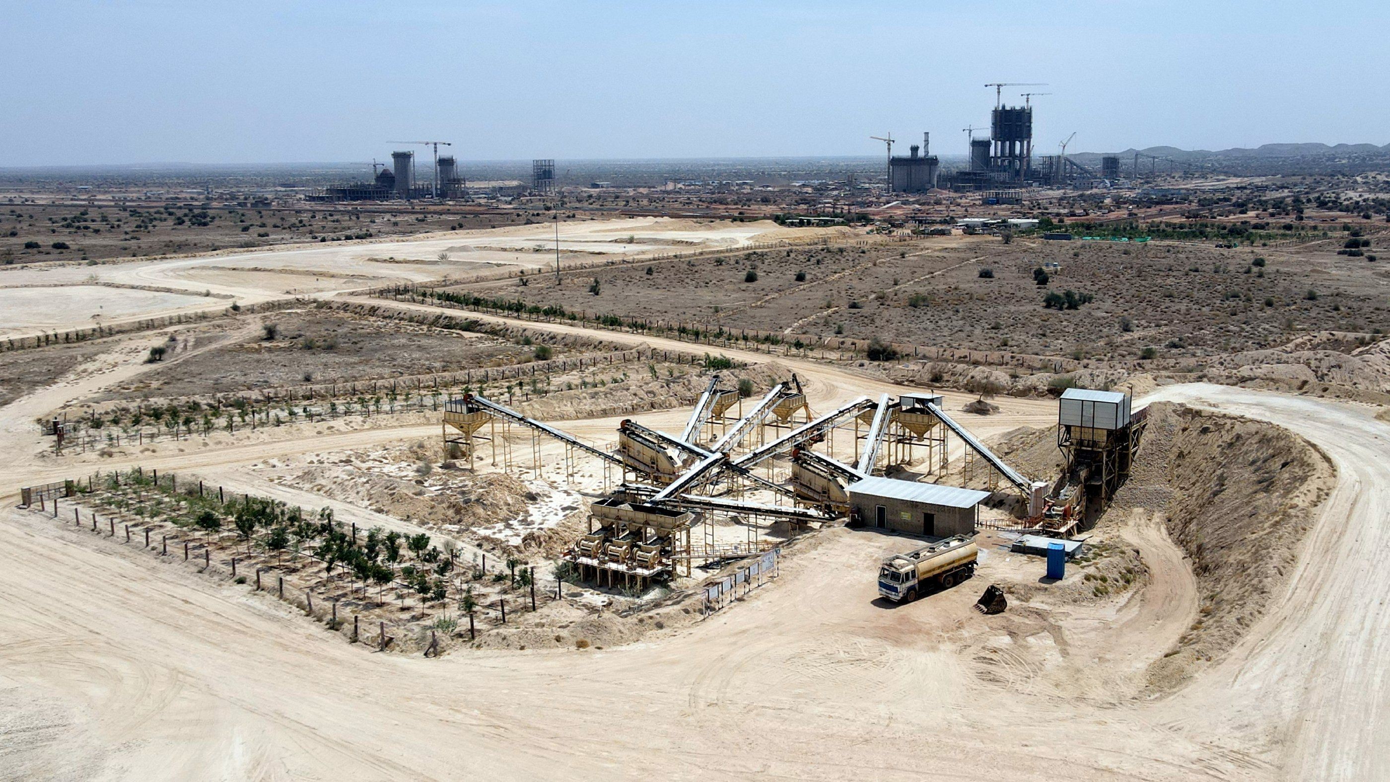 Aerial view shows an industrial quarry with machinery and trucks in a dry, expansive desert.