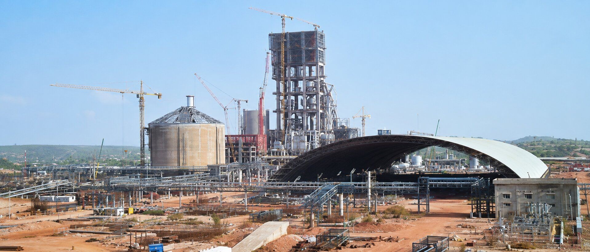 Large industrial complex under construction with tall structures, silos, and cranes under a clear sky.