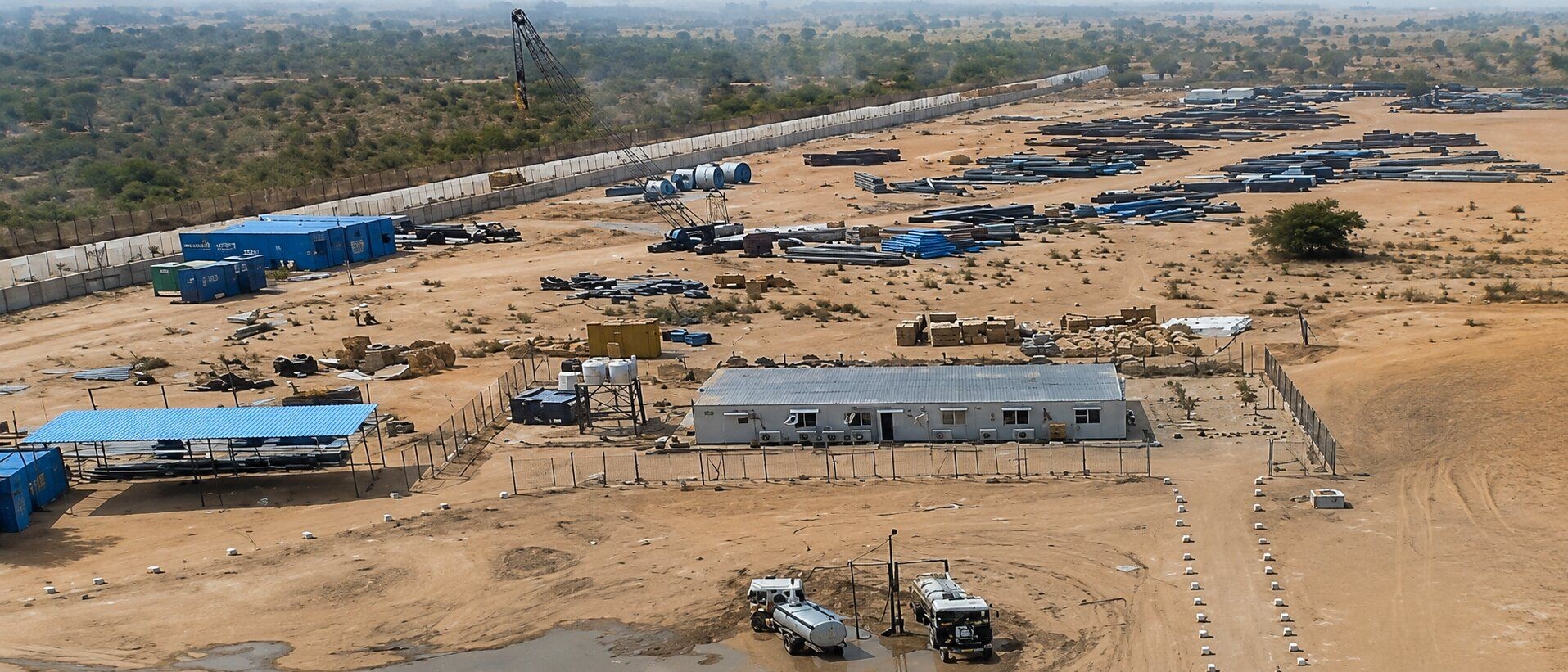 Aerial view of an industrial site featuring modular buildings and vehicles on sandy ground.