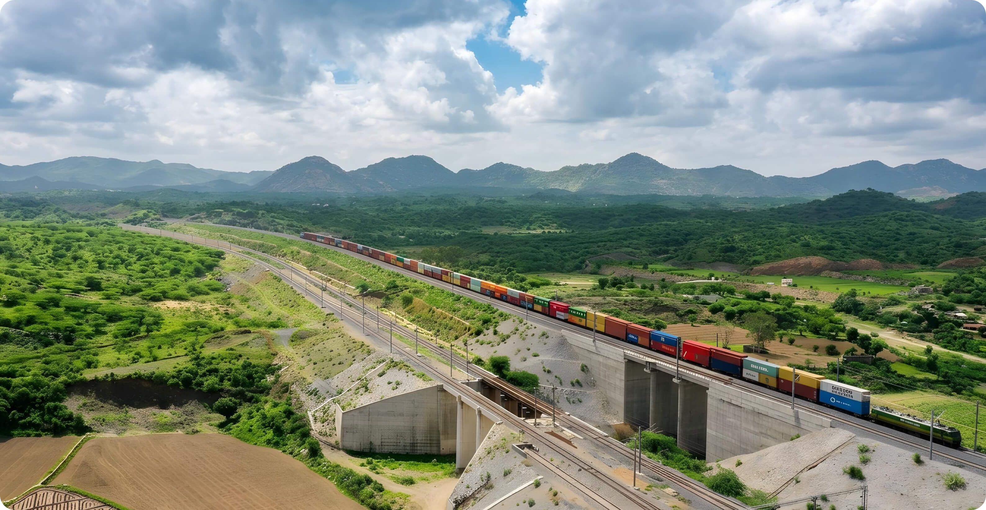 Long freight train with colorful containers travels through a lush green mountainous landscape.