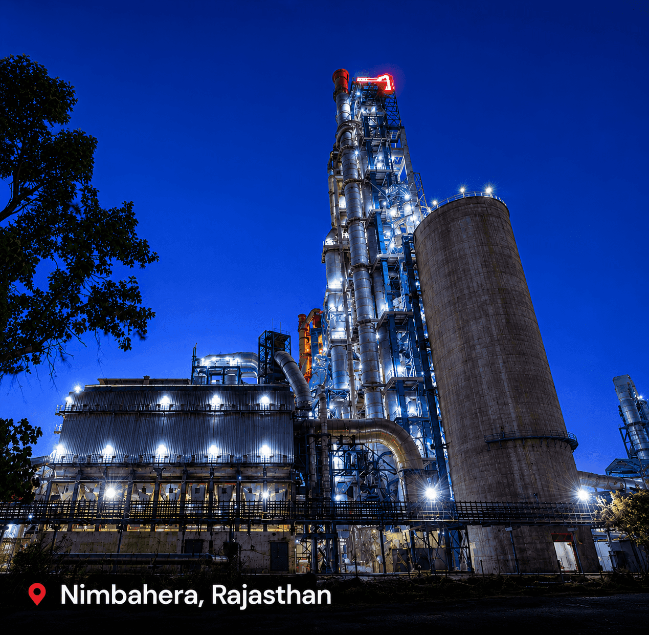 Large industrial plant with tall structures brightly lit against a dark blue night sky.