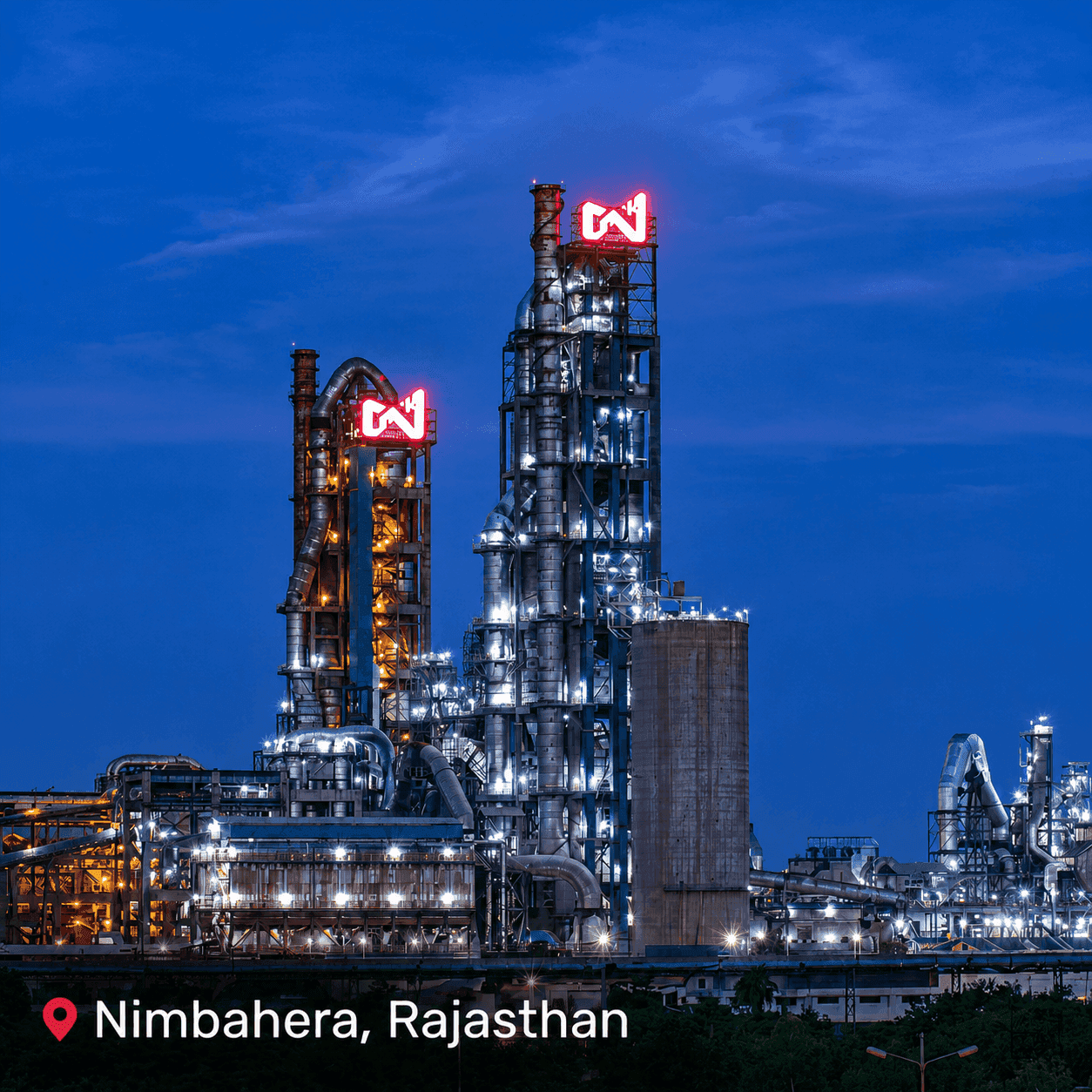Large industrial plant with glowing 'N' logos illuminated at night under a dark sky.