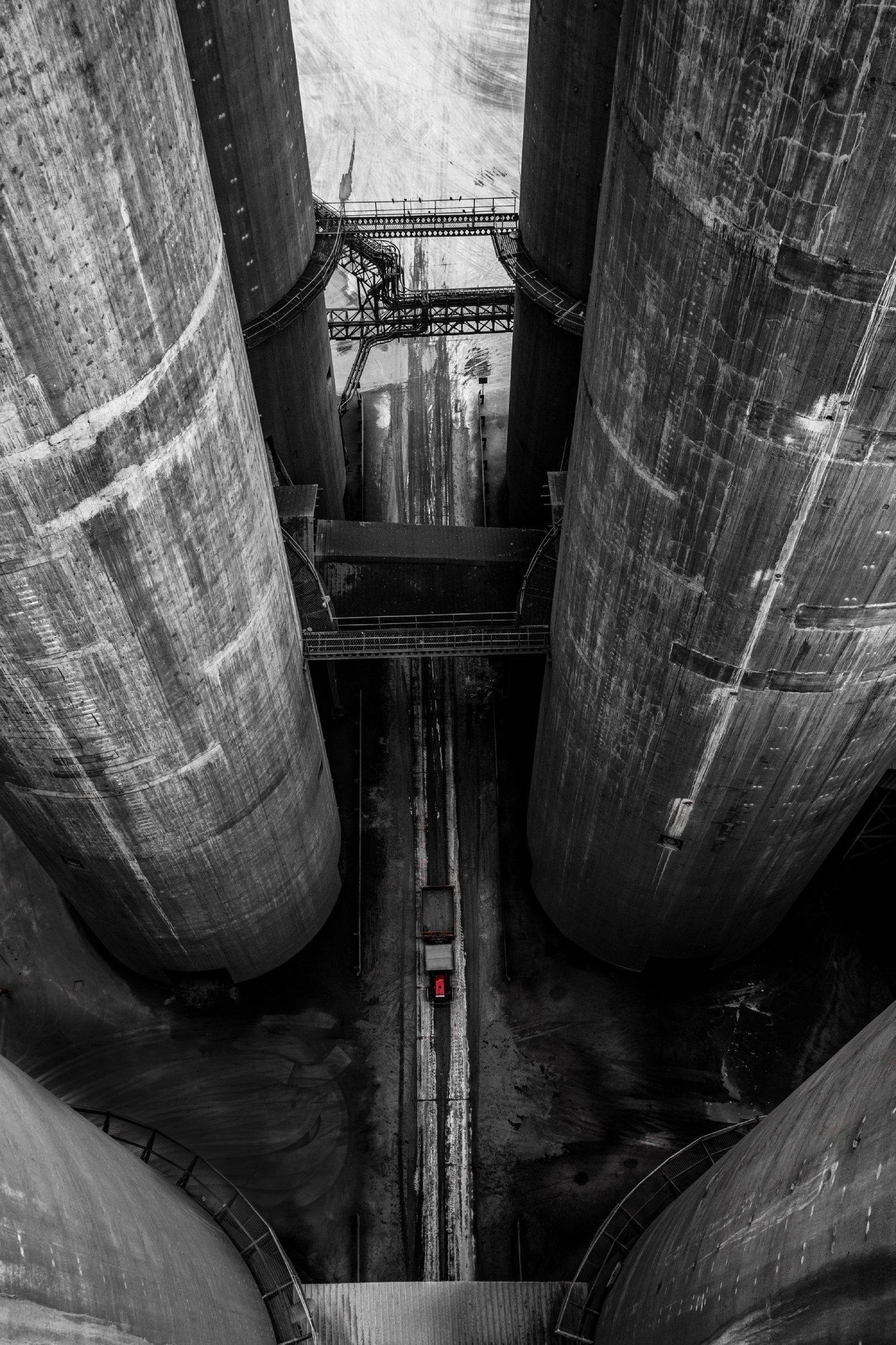Low-angle view looking up between two massive industrial pipes in black and white.