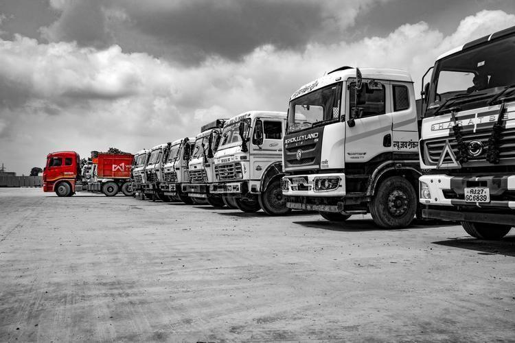 A long line of industrial trucks, with one distinct red truck visible in the distance.