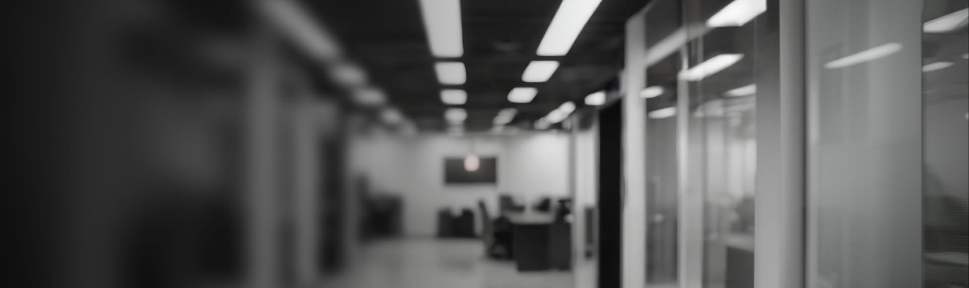 Blurred black and white modern office hallway with glass walls and bright lights.